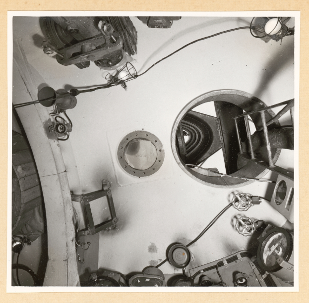 Ein Schwarz-Weiß-Foto eines unordentlichen Raumes voller verschiedener Geräte, darunter eine Kameralinse und Drähte.