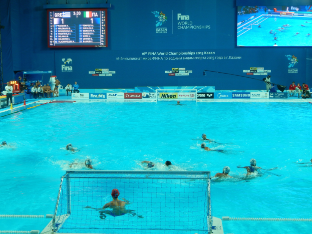 Gruppe von Athleten, die Wasserball in einem Pool während der FINA-Weltmeisterschaften 2016 in Kazan spielen, mit einem Netz, das den Pool teilt, und Zuschauern auf der linken Seite.