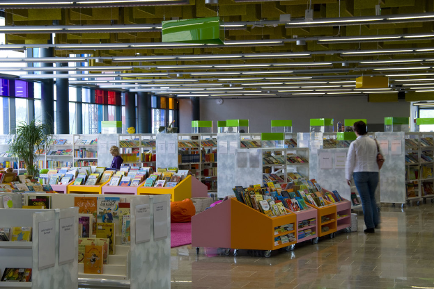 Ein Mann steht in einer Bibliothek mit Büchern auf Regalen, einer Pflanze und Papieren mit Text an den Regalen.