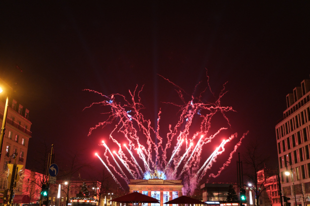 Eine belebte Straßen Szenerie am Silvesterabend in Berlin, voller Menschen, Fahrzeuge und festliche Lichter von Gebäuden und Feuerwerk.