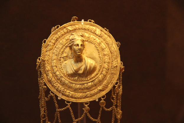 Goldene Medaille mit einem Frauengesicht auf dunklem Hintergrund, mit feiner und luxuriöser Verzierung.