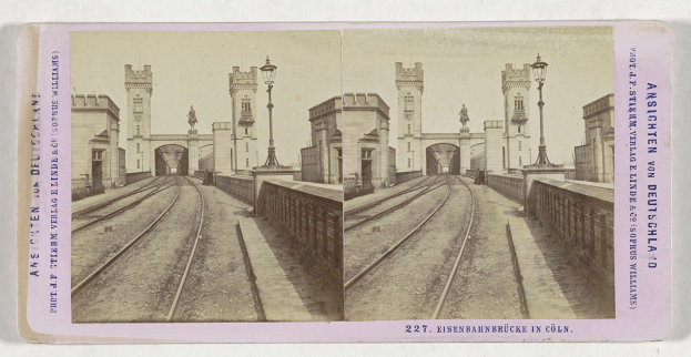 Schwarz-weißes stereoskopisches Foto einer Eisenbahnbrücke in Köln, Deutschland, das Eisenbahninfrastruktur, Umgebungswände, Pfosten, Statuen, Himmel und Text zeigt.