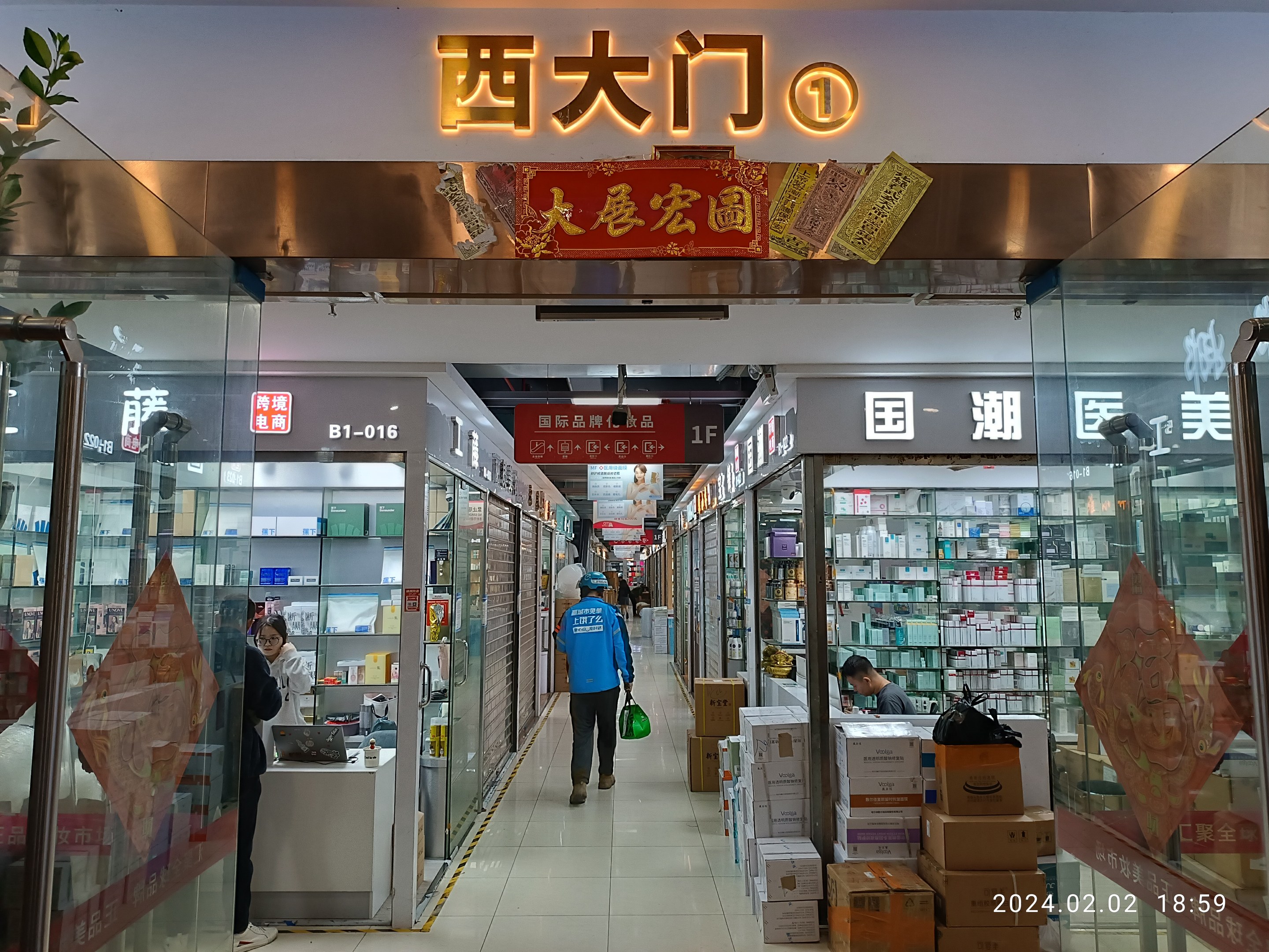 Innenansicht einer chinesischen Apotheke mit Glaswänden, Regalen mit Artikeln, verstreuten Kartons, einer Pflanze links und einer Namensschilder oben.