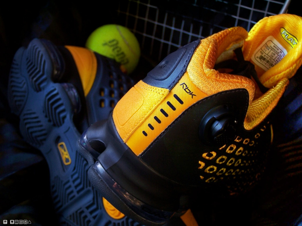 Ein Schuhpaar und ein Ball befinden sich in der Mitte des Bildes, im Hintergrund ist ein Zaun zu sehen.