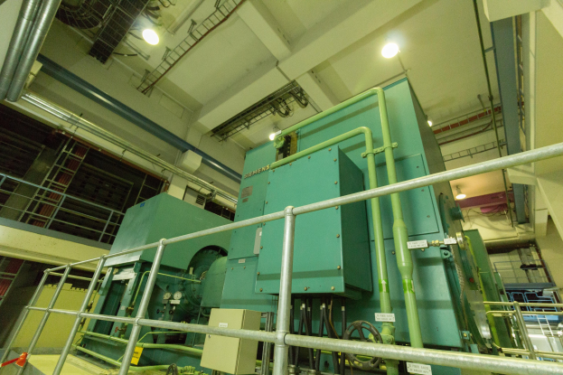 Großer industrieller Wärmetauscher mit umfangreichen Rohrleitungen und Ventilen in einem Gebäude, umgeben von Geländern.