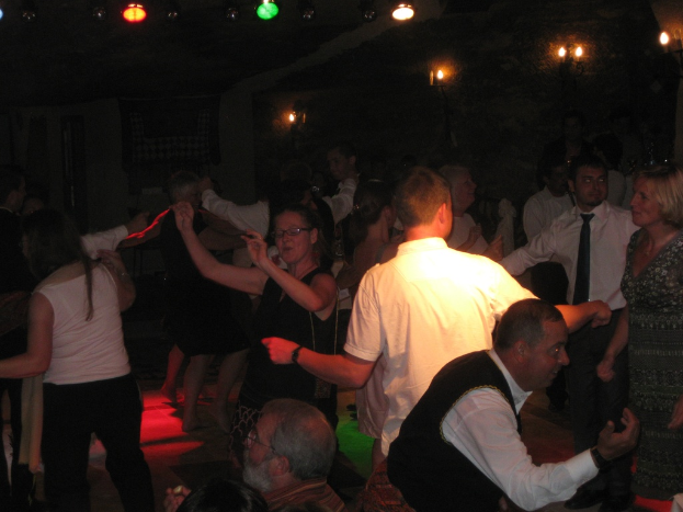 Eine lebhafte Partyszene mit tanzenden Menschen auf dem Boden unter einer dunklen Decke, die mit verschiedenen bunten Lichtern geschmückt ist.