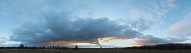 Ein bewölkter Himmel mit einem Fabrikschornstein, der Rauch ausstößt, und ein paar Bäumen und Pflanzen auf der rechten Seite.