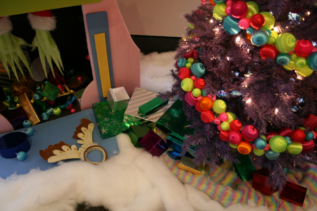 Drinnen, ein geschmückter Weihnachtsbaum rechts, Geschenkboxen und Décor in der Mitte, eine Hütte mit Décor oben links und Baumwolle und Wolle unten.