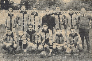 Ein Schwarz-Weiß-Foto einer Fussballmannschaft, bei der einige Spieler stehen und andere in einer Hockposition sind, mit Text unten.