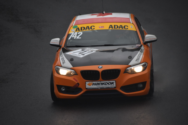 Oranges BMW-Rennfahrzeug mit sportlichem Text und Zahlen auf einer Rennstrecke.