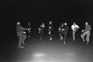 Eine Gruppe von Männern auf einer Bühne in Schwarz-Weiß-Einstellung, die Schuhe tragen, was darauf hindeutet, dass sie mitten in einer Performance sind.