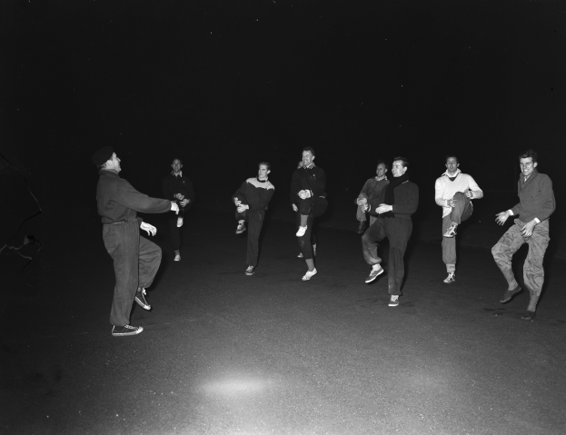 Eine Gruppe von Männern auf einer Bühne in Schwarz-Weiß-Einstellung, die Schuhe tragen, was darauf hindeutet, dass sie mitten in einer Performance sind.