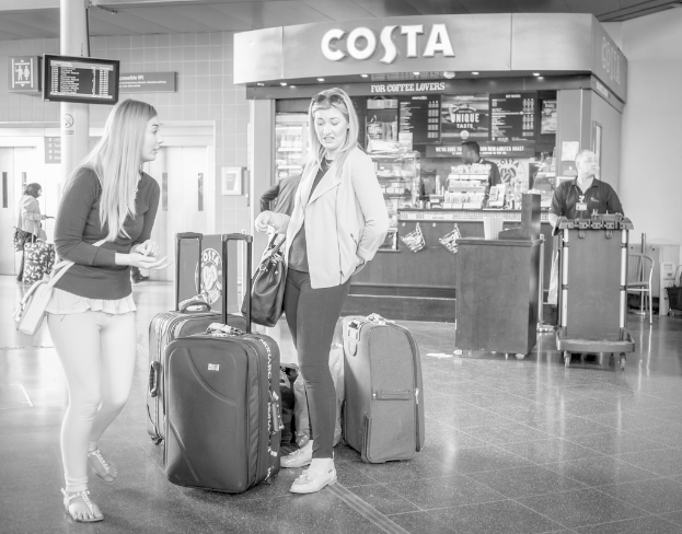 Zwei Frauen mit Gepäck vor einem Café an einem Ort, der wie ein Flughafen aussieht.