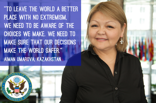 Eine Frau in einem schwarzen Kleid steht vor einem Fenster mit einer Aussage über die Weltverbesserung, mit sichtbaren Flaggen im Hintergrund.