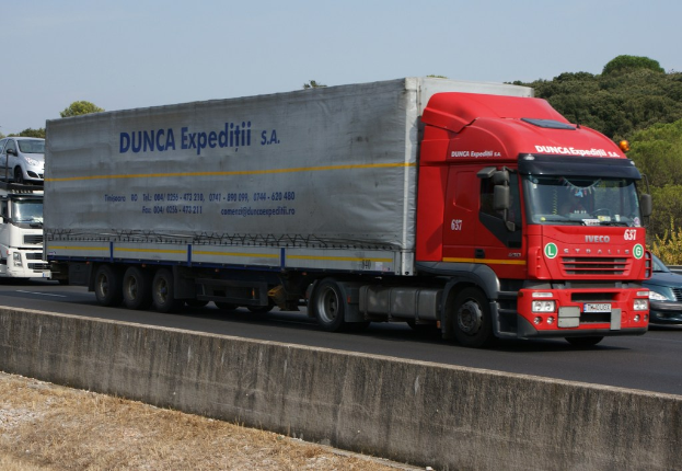 Ein Lastwagen fährt auf einer Straße mit anderen Fahrzeugen und Bäumen im Hintergrund.