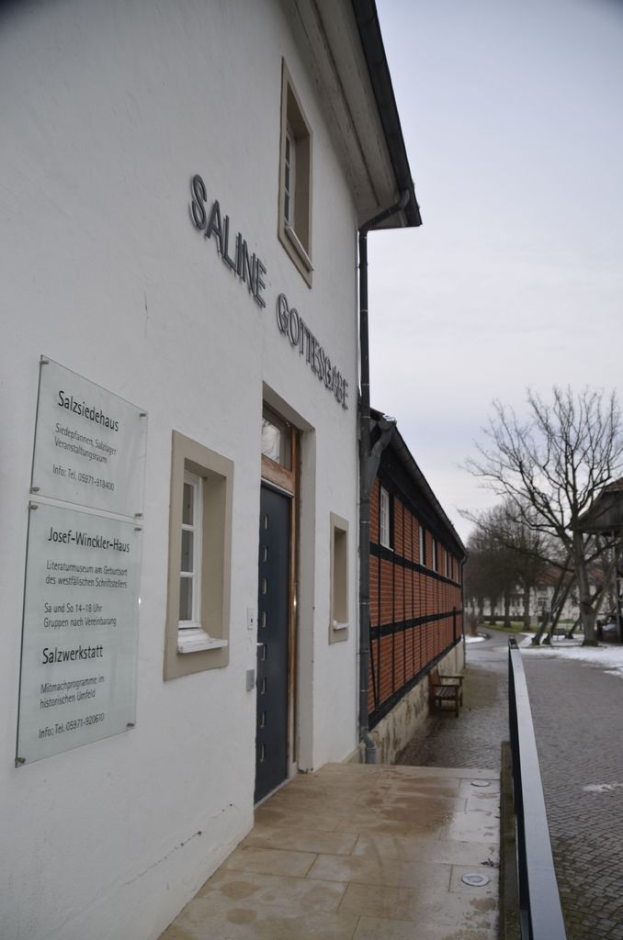 Ein Gebäude mit Fenstern, Text und Glasplatten auf der linken Seite, einem Geländer und einer Straße in der Mitte und Bäumen, einem Schuppen und Himmel im Hintergrund.