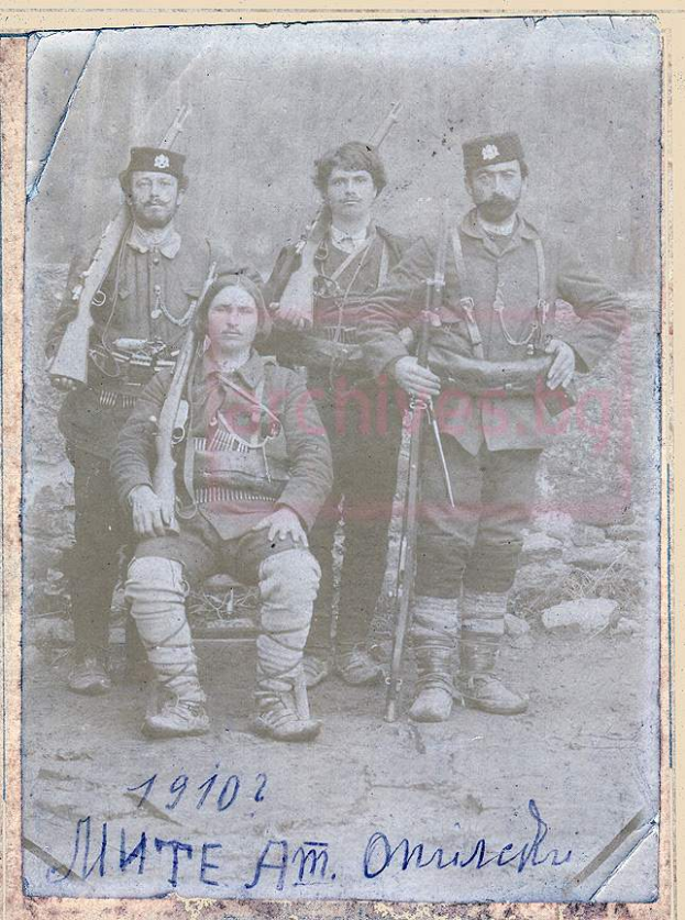 Ein Schwarz-Weiß-Foto einer Gruppe von Männern in Militäruniformen, einer sitzend mit einer Waffe in der Hand, mit dem Text "1910-1902 - munte am omisch" unten.