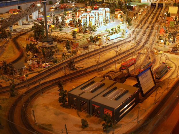 Eine detaillierte Modelleisenbahn-Ausstellung in einem Museum, mit Gebäuden, Bäumen, Schienen, Fahrzeugen, Polen, Lichtern und Schildern, die eine belebte Stadtlandschaft darstellen.