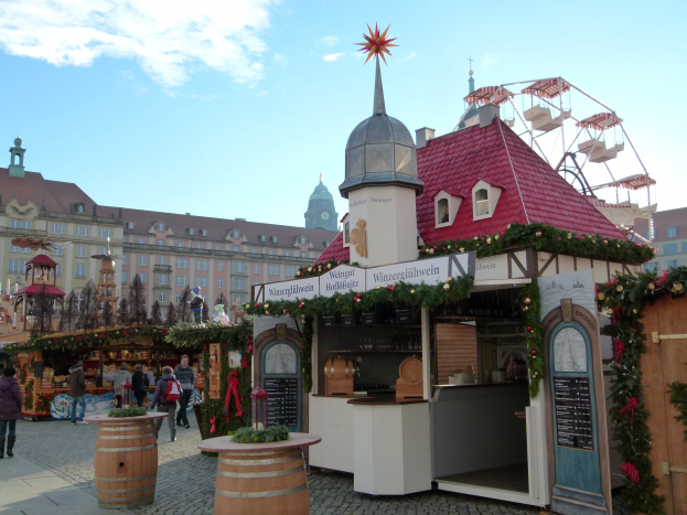 Ein geschäftiger Weihnachtsmarkt in Nürnberg, Deutschland mit Menschen um dekorierte Stände, festliche Lichter, Schmuck, Gebäude, ein Riesenrad und einen bewölkten Himmel, mit einer Tafel mit Text auf der rechten Seite.