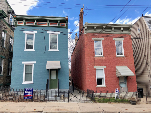Eine Reihe bunter Häuser an einer Straßenecke mit einem Mietschild, auf dem "Mietwohnungen zu vermieten, Listid 29058910, Lage 5901 S Elmwood Ave Chicago 60618" steht, Metallzaun, Topfpflanzen, ein Müllcontainer, Drähte und ein bewölkter Himmel.