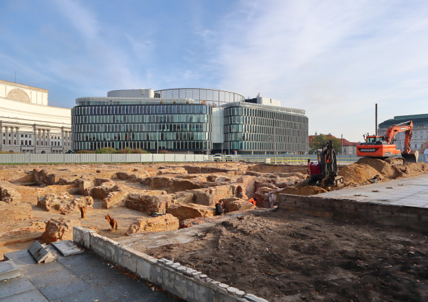 Eine Baustelle in Berlin, Deutschland, mit einem großen Gebäude im Hintergrund, umgeben von Fahrzeugen, Menschen, Felsen, Erde, Wänden, Pfählen, Bäumen und anderen Gegenständen unter einem bewölkten Himmel während des Baus der Berliner Mauer.