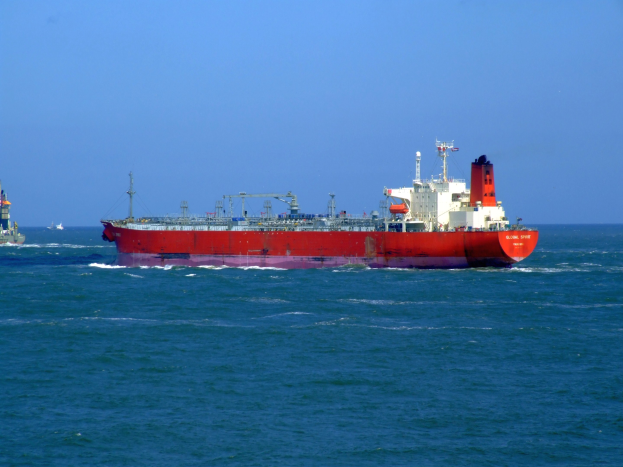Ein großes rotes und weißes Öltankschiff auf dem Meer mit anderen Schiffen im Hintergrund unter einem klaren blauen Himmel.