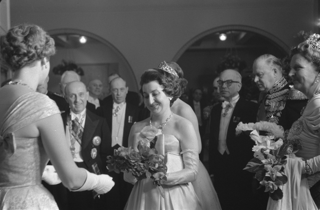 Schwarzes und weißes Foto von Queen Elizabeth II. und Prinz Philip, Duke of Edinburgh, an ihrem Hochzeitstag, die Kronen tragend und Blumensträuße haltend, umgeben von einer Gruppe von Menschen, mit Lichtern und einer Wand im Hintergrund.