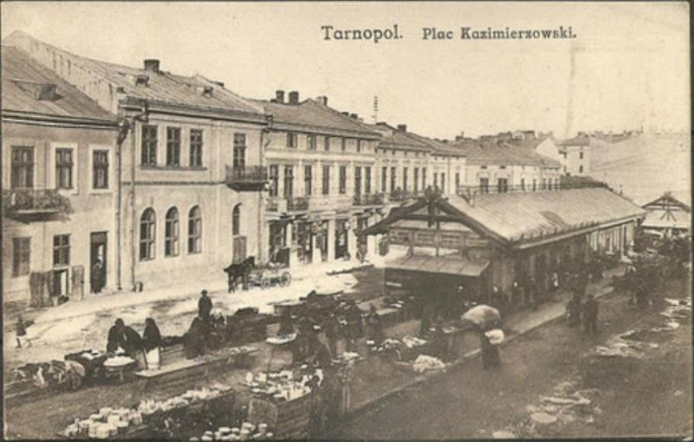 Schwarz-weiß-Foto eines belebten Marktes in Tarnopol, Polen mit Menschen und Karren sowie Gebäuden im Hintergrund.