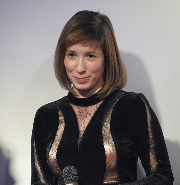 Frau in schwarzem Kleid mit Mikrofon während eines BBC Radio 1-Interviews vor einer Wand mit selbstbewusstem Gesichtsausdruck.