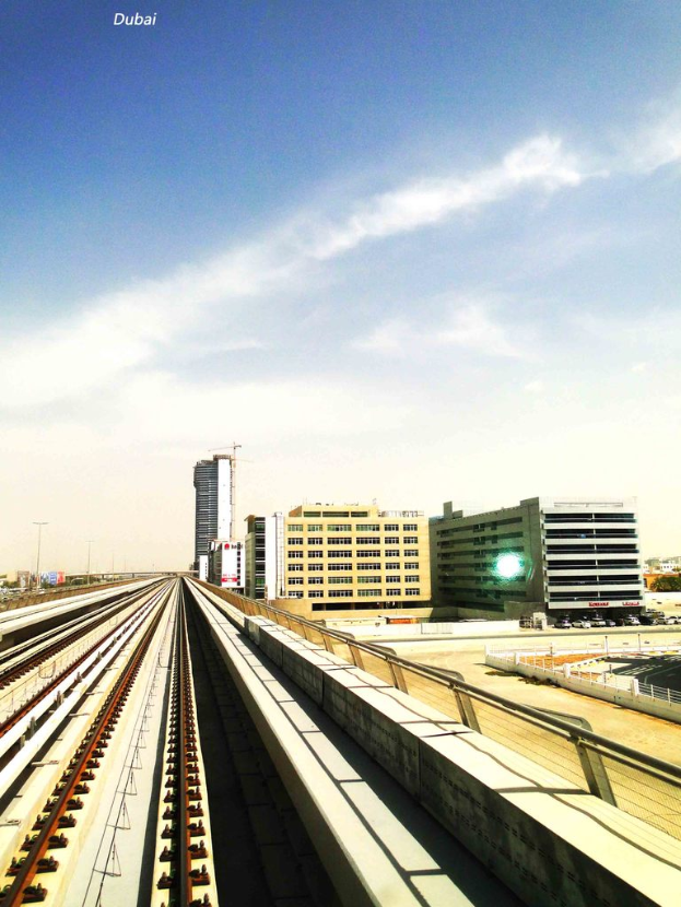 Eisenbahnschienen in der Mitte, Gebäude und Straßen rechts, mit einem Himmel und Wolken im Hintergrund.