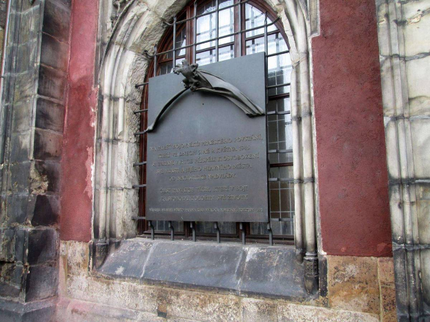 Ein steinernes Gebäude mit einem Fenster und einer Gedenktafel für die Opfer des Holocaust mit eingravierter Inschrift.