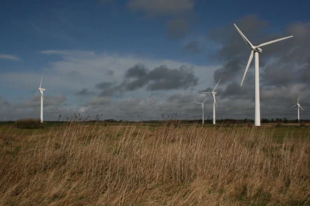 Ein Windkraftwerk im Grünen mit Bäumen im Hintergrund und Wolken am Himmel, mit Text, der den Standort als Niederlande angibt.
