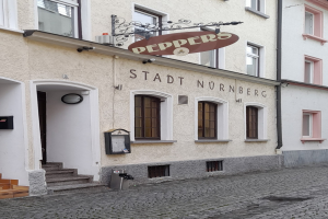 Gebäude mit einer "Stadt Nurnberg"-Aufschrift, Treppe zum Eingang, Fenstern, einer Tür und einem Müllcontainer im Vordergrund.