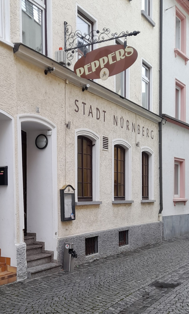 Gebäude mit einer "Stadt Nurnberg"-Aufschrift, Treppe zum Eingang, Fenstern, einer Tür und einem Müllcontainer im Vordergrund.