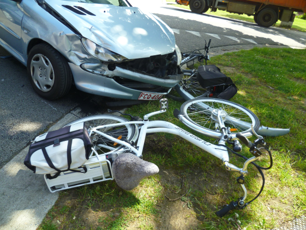 Ein Auto krachte auf der Straßenseite mit einem Fahrrad in der Nähe, Bäume und ein klarer blauer Himmel im Hintergrund.