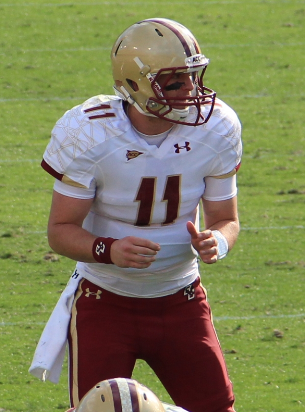 Ein Mann in einer Football-Uniform und einem Helm steht auf einem grasbewachsenen Feld, bereit als Quarterback.