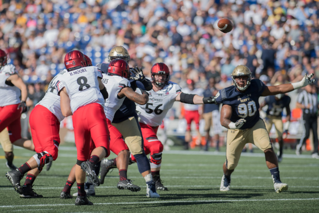 Gruppe von Menschen in Helmen und Schuhen, die Fußball auf einem Feld mit einem Ball in der Luft spielen.