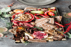 A tray with Christmas treats like pomegranates, candies, and other food items, alongside two glasses and a plate on the floor.