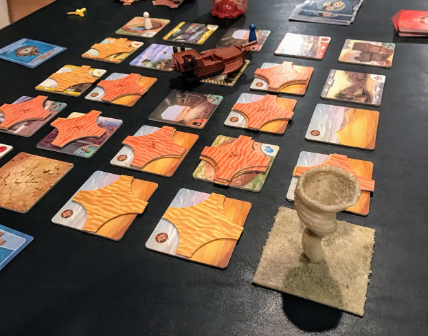 Ein vollgestellter Tisch mit Star Wars: The Old Republic-Spielkarten, Spielzeugen und Gegenständen in einem Raum mit einer Wand im Hintergrund.