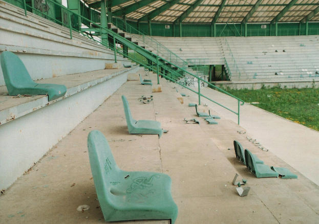 Ein Stadion mit verstreuten Stühlen, grasigem Boden und sichtbaren Stufen, die nach oben führen.