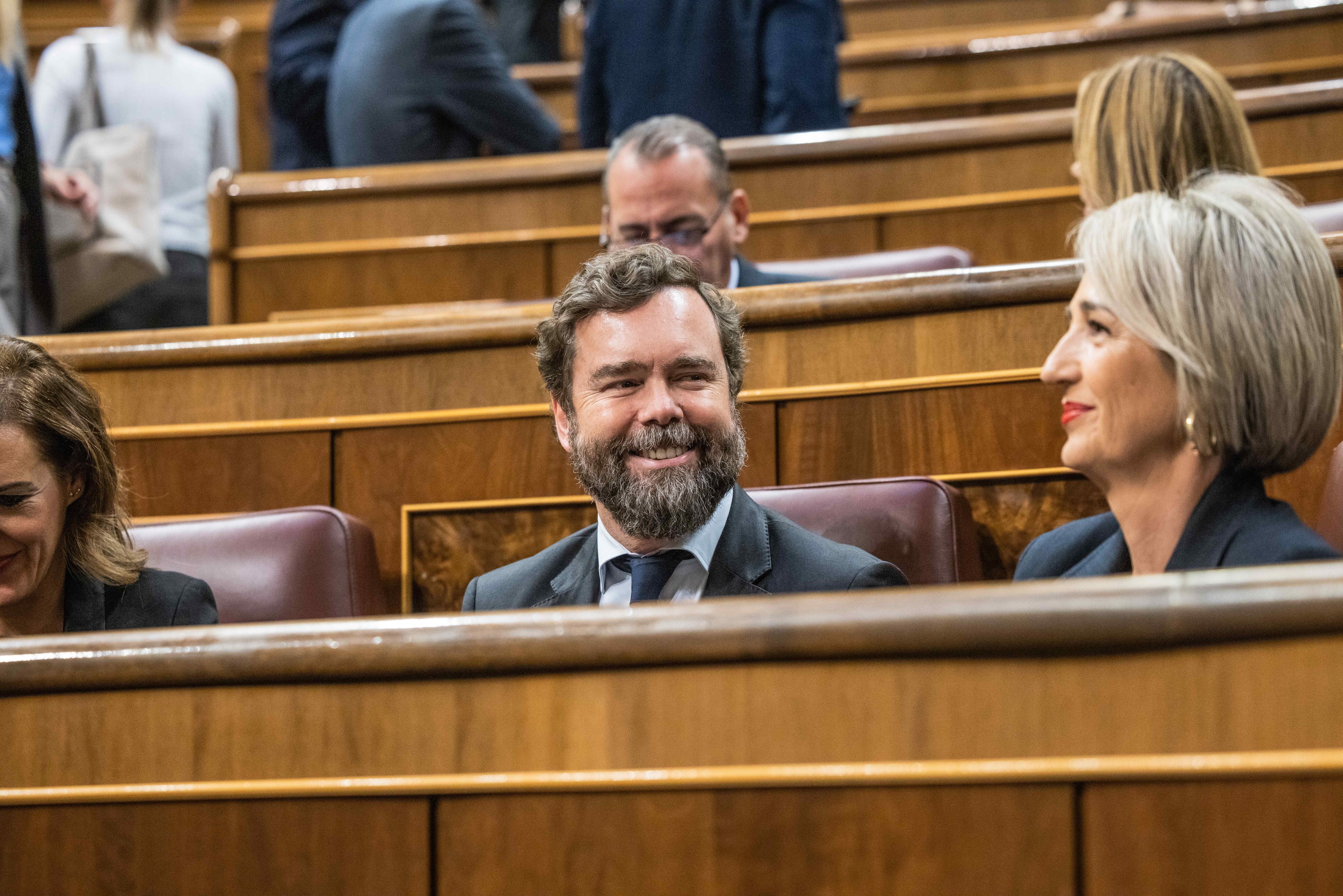 Ein Mann in einem Anzug und zwei leger gekleidete Frauen sitzen zusammen in einem Gerichtssaal mit Bänken im Hintergrund.