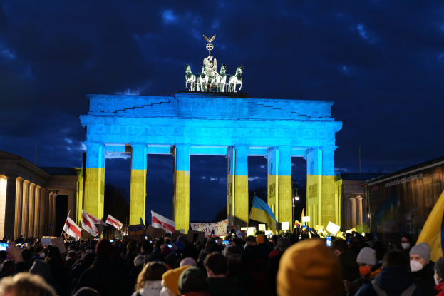 Eine Menschenmenge steht vor dem Brandenburger Tor in Berlin, Deutschland, mit Fahnen und Schildern, einem Banner auf der rechten Seite und Wolken am Himmel.