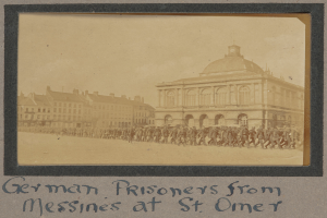Eine Gruppe deutscher Gefangener aus Messines steht vor einem Gebäude mit einem klaren blauen Himmel im Hintergrund, mit Text am unteren Bildrand.