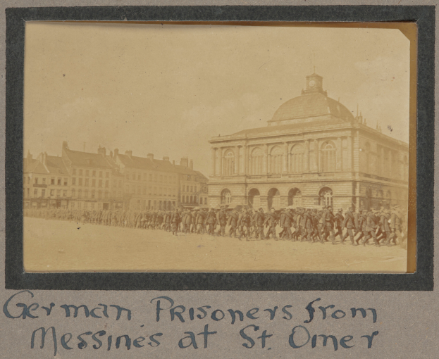 Eine Gruppe deutscher Gefangener aus Messines steht vor einem Gebäude mit einem klaren blauen Himmel im Hintergrund, mit Text am unteren Bildrand.