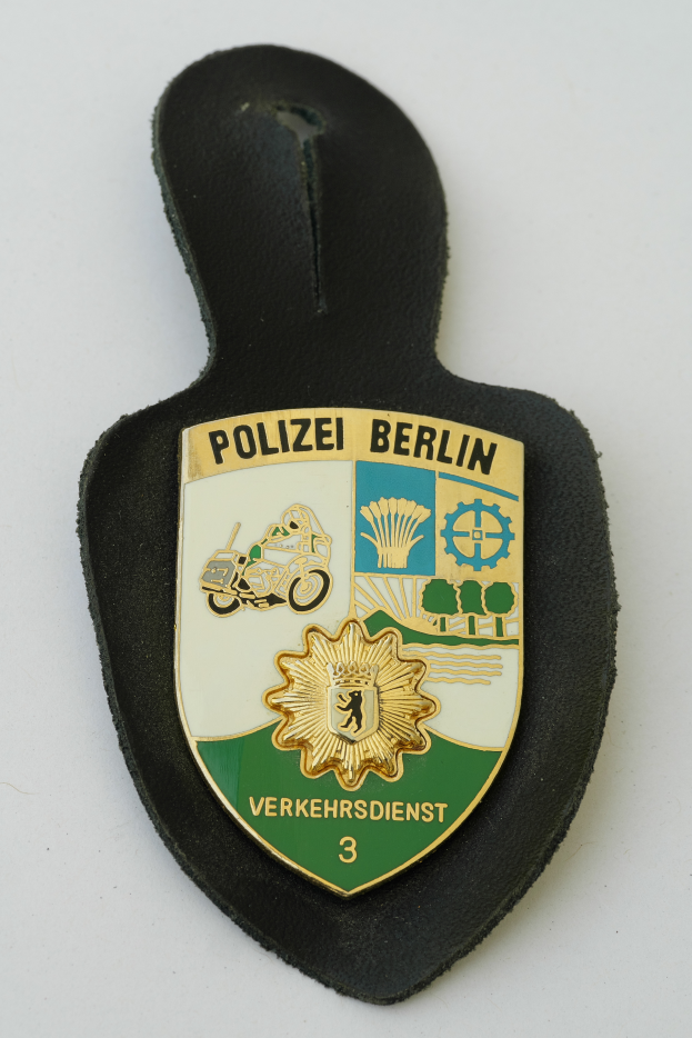 Ein Polizeistern mit der Aufschrift "Polizei Berlin", der ein blaues Schild mit einem weißen Stern in der Mitte und einen weißen Rand hat.
