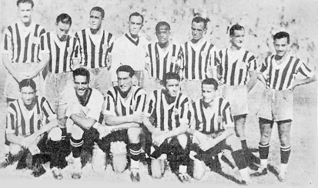 Ein Schwarz-Weiß-Foto einer Fußballmannschaft, mit einigen Spielern, die stehen und andere, die auf dem Boden sitzen, und Text unten.