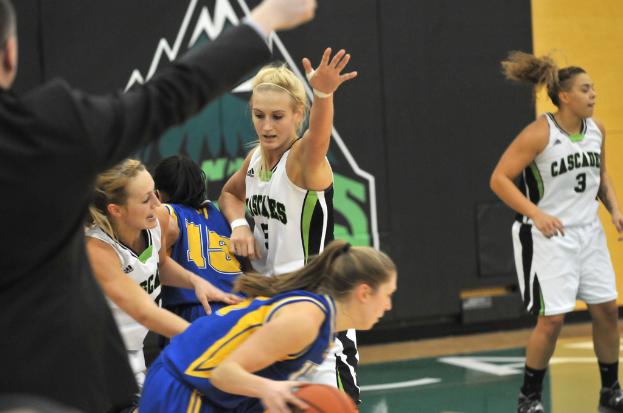 Mehrere Mädchen spielen Basketball auf einem Platz, wobei ein Mann auf der linken Seite steht.