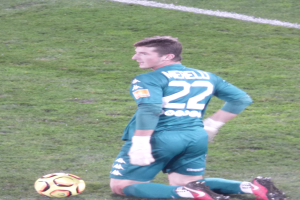 Ein Fußballspieler sitzt auf dem Boden mit einem Fußball vor ihm, trägt eine Sportuniform und Schuhe.