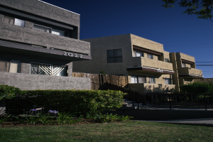 Eine Reihe von Wohngebäuden in San Francisco, Kalifornien, mit Fenstern, Pflanzen, Gras, einem Zaun, Treppen, einem Baum, Drähten und einem Himmel im Hintergrund.