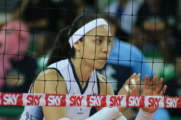 Frau im Volleyballspiel auf einem Feld, die eine Uniform trägt, mit einem Netz im Vordergrund und einem unscharfen Hintergrund.